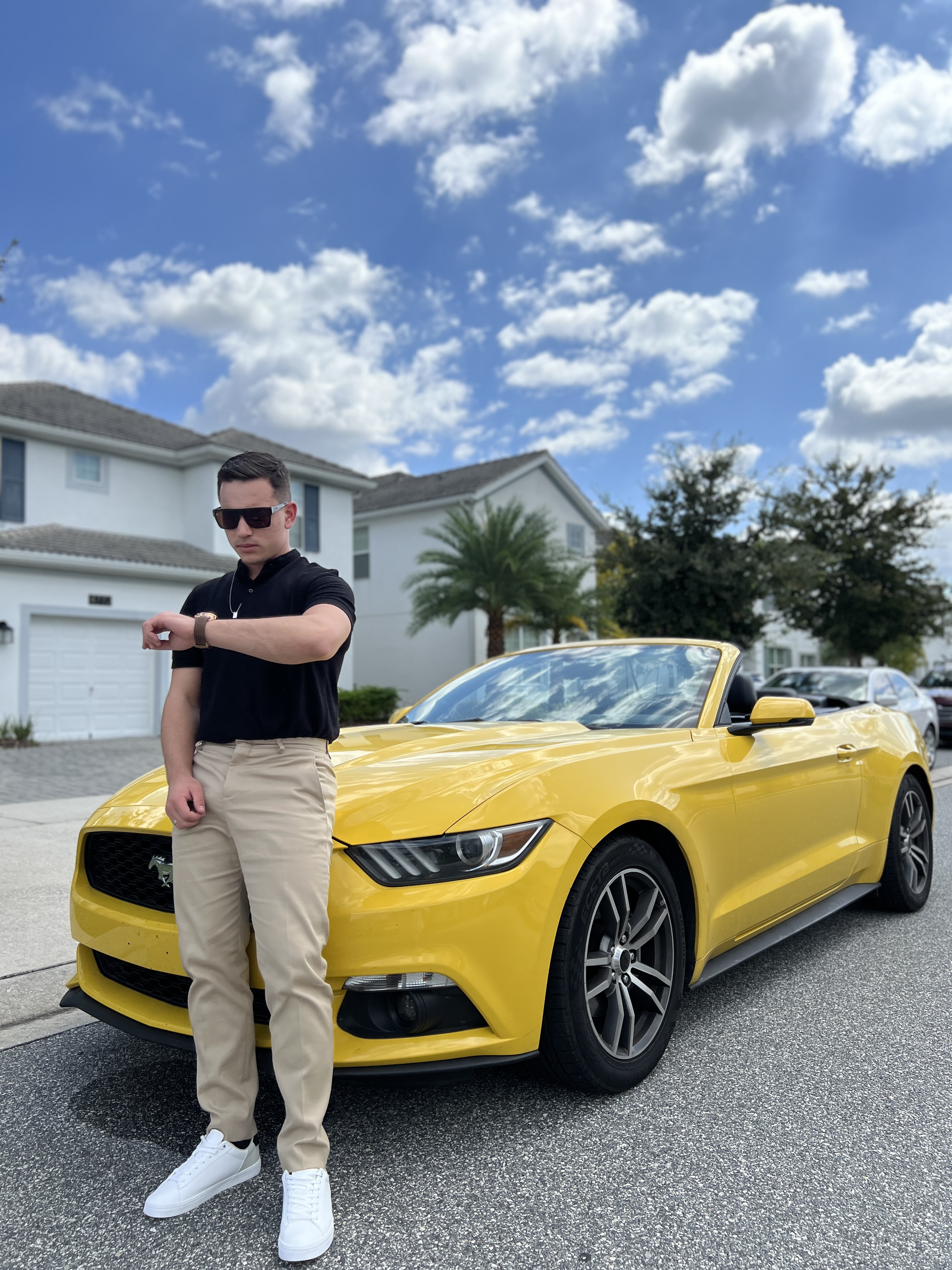 Homem de camisa preta ao lado de carro esportivo amarelo